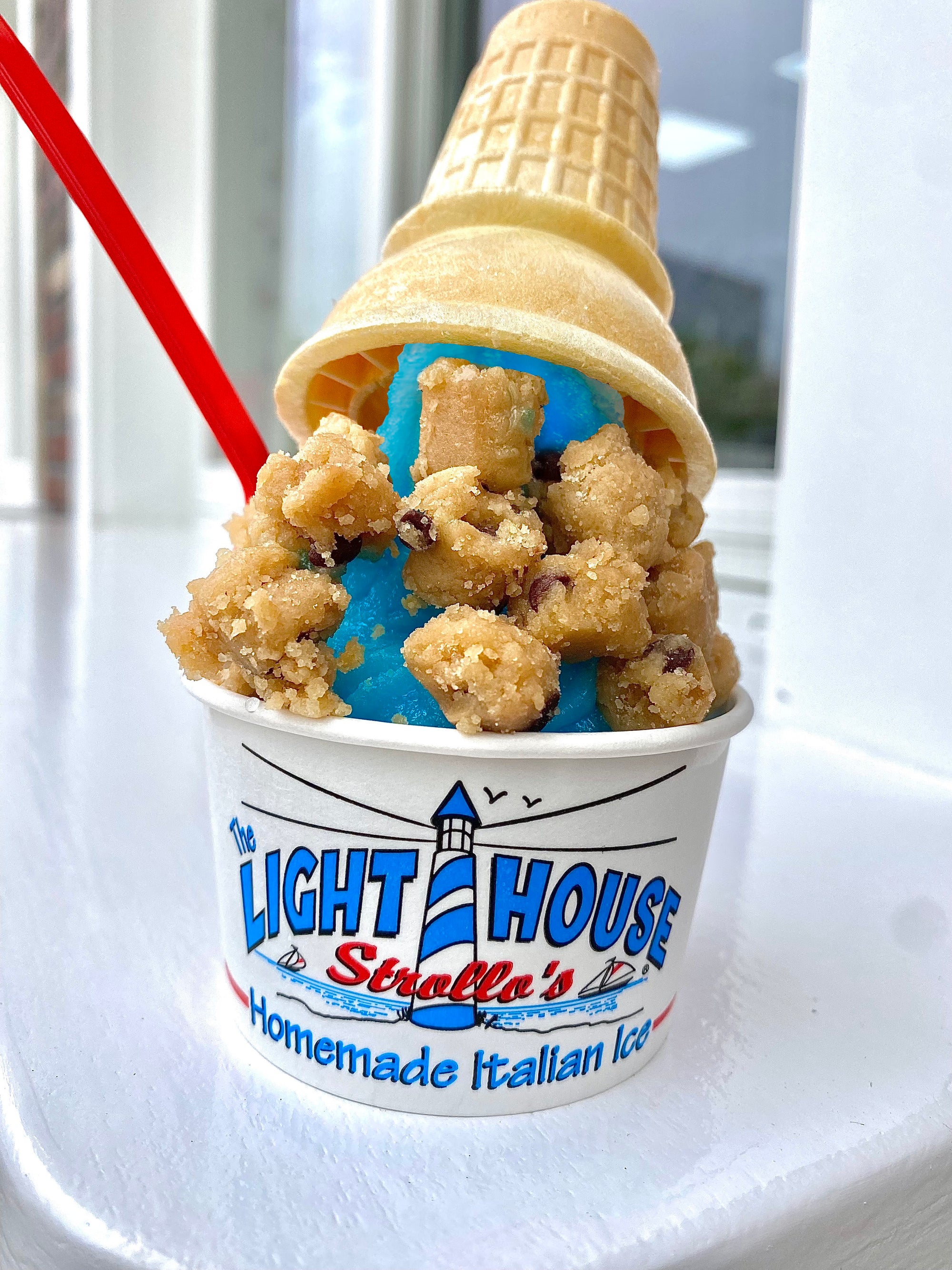 A Strollo's Lighthouse cup with blue raspberry homemade Italian Ice topped with cookie dough and a wafer cone